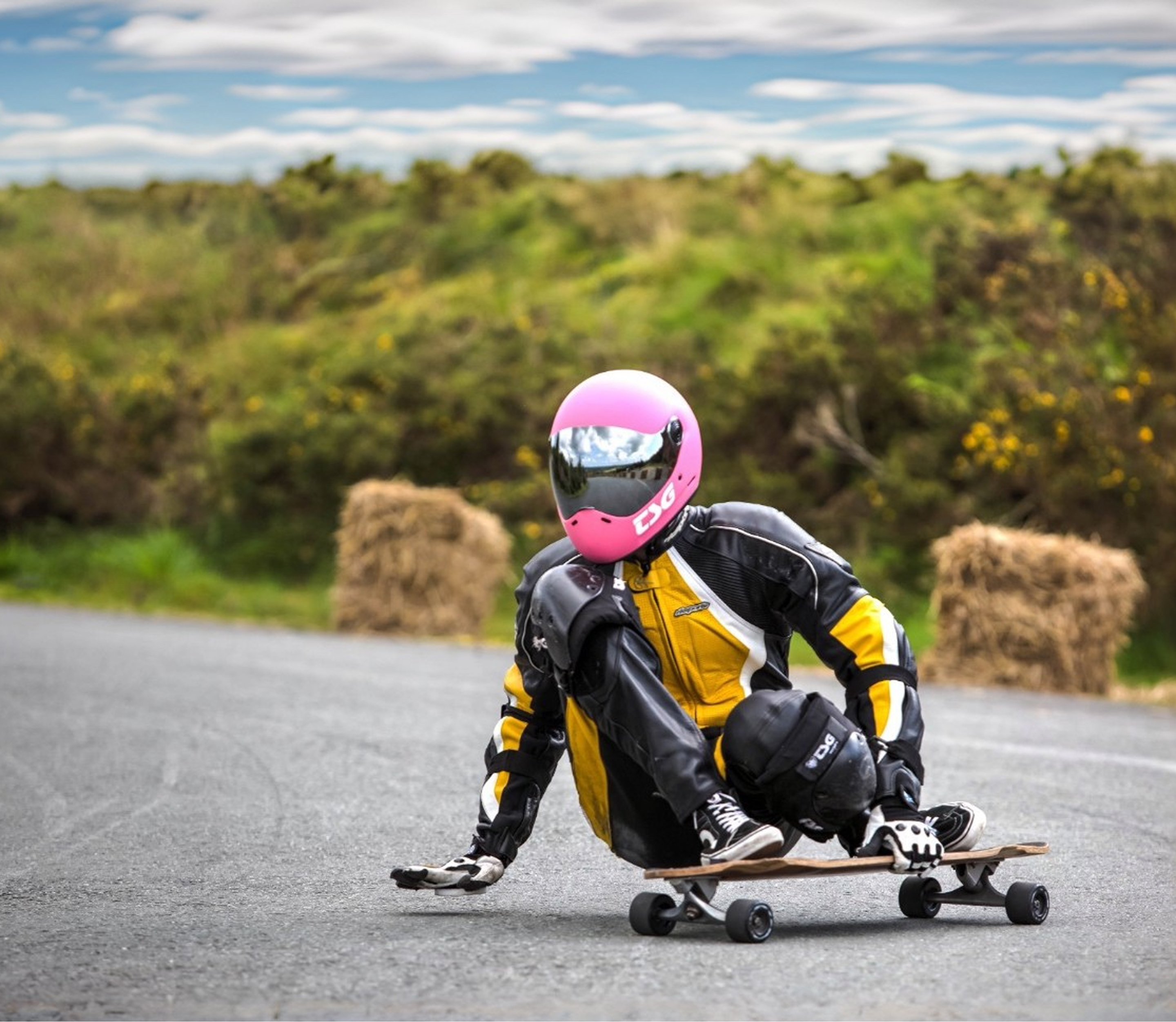 Downhill longboarder in a leather suit and pink helmet sliding on a mountain road