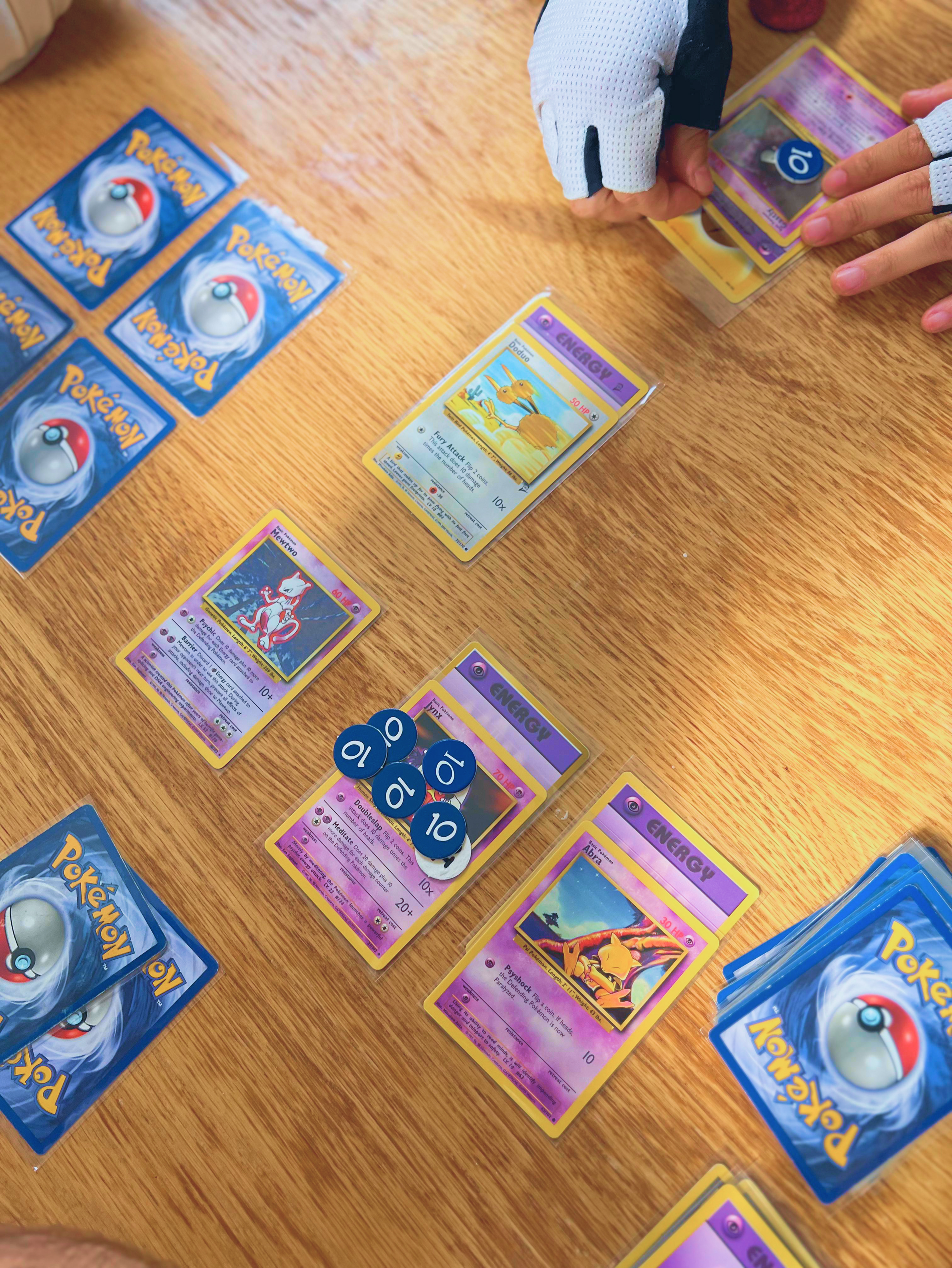 Pokémon Trading Card Game match with Mewtwo, Jynx, Abra, and Doduo on a wooden table